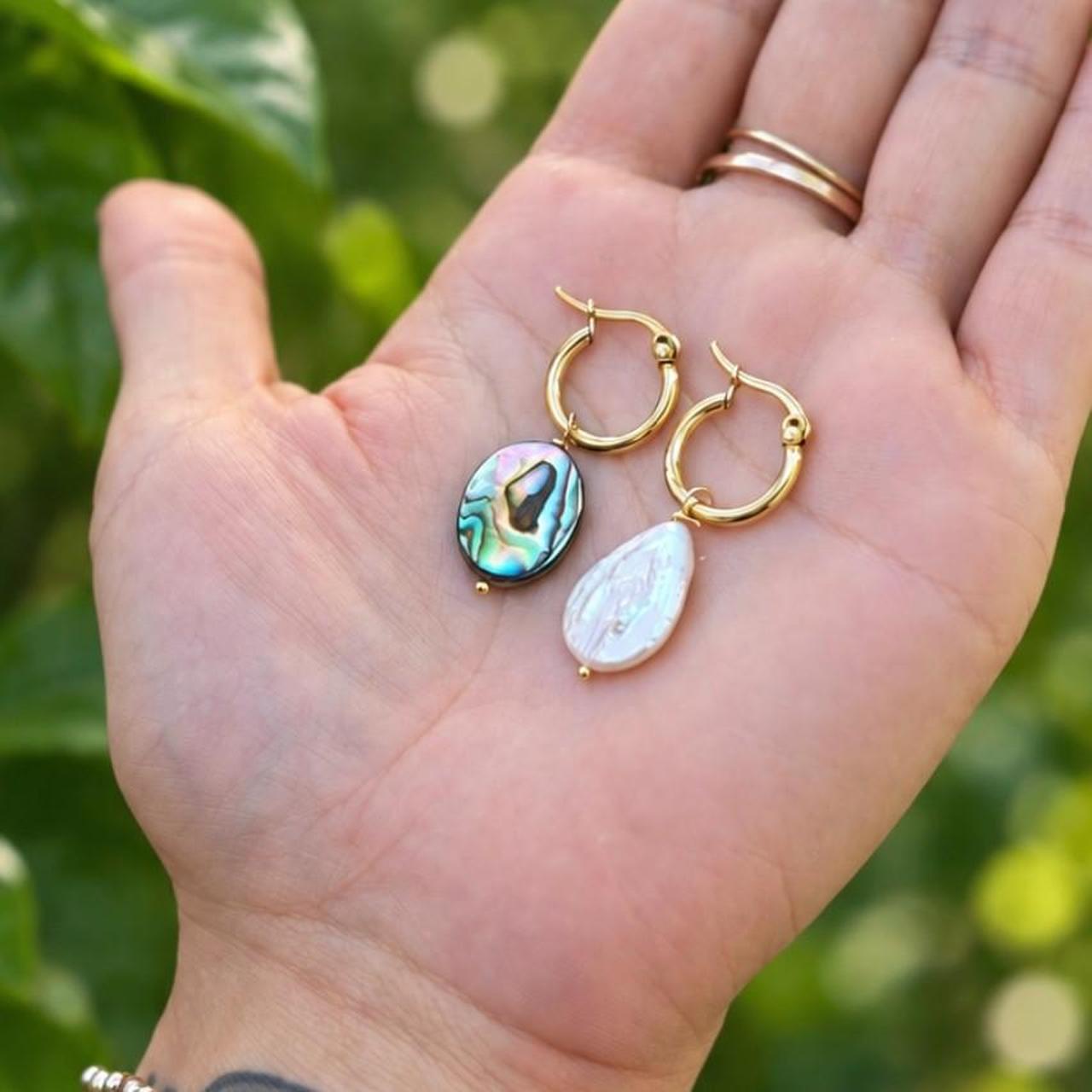 Gold hoops with an iridescent abalone drop and a white pearl drop resting in a hand